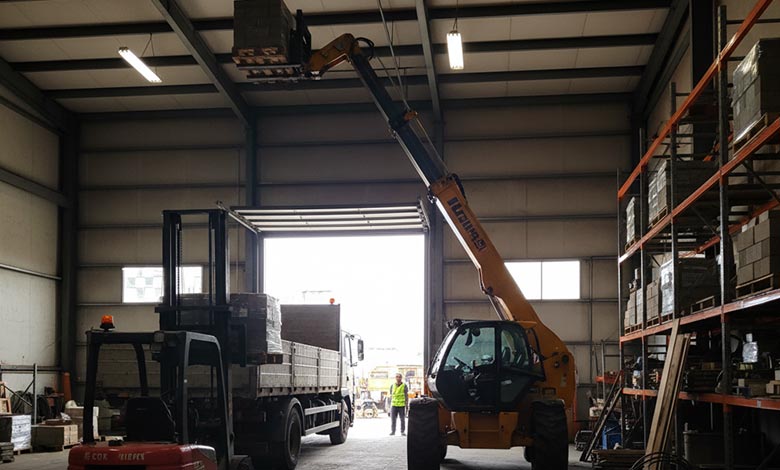 A rough terrain forklift efficiently moving pallets next to a telehandler placing bricks on a second-story building