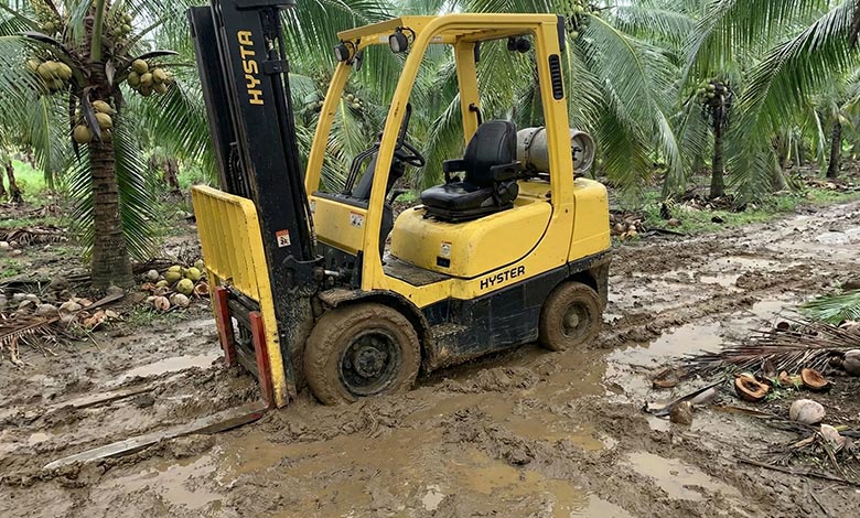 A standard warehouse forklift hopelessly stuck in mud, its smooth tires covered.