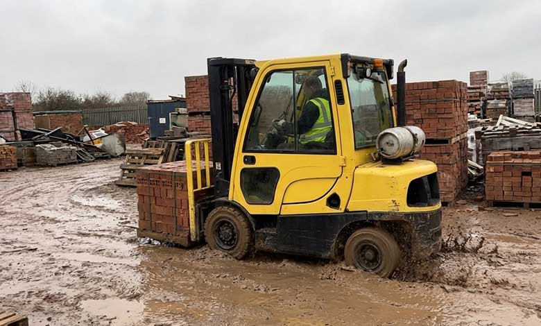 Standard Forklift Failed in Muddy Brick Yard A standard warehouse forklift stuck in the mud of a brickyard, its wheels spinning uselessly.