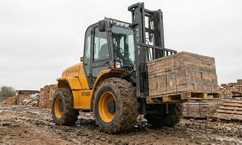 BLANC-ELE Rough Terrain Forklift in Brick Yard A heavy-duty BLANC-ELE forklift effortlessly lifting a heavy pallet of bricks in a cluttered, uneven brickyard.